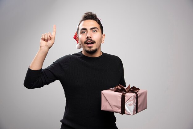 A young man in a Santa's hat showing a finger up and holding a gift .