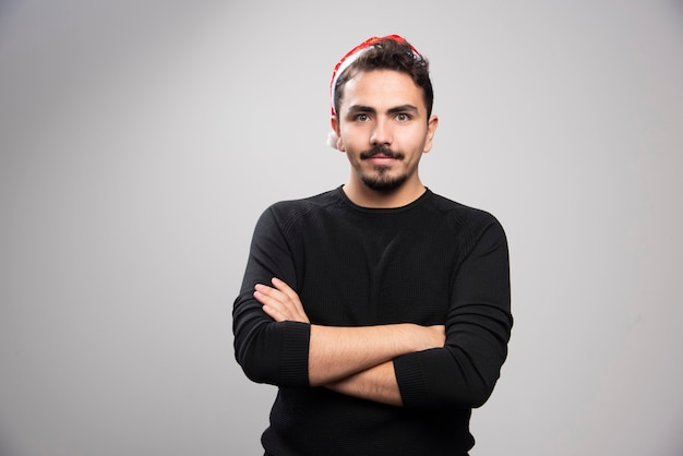 회색 벽 위에 서있는 산타의 빨간 모자에서 젊은 남자.