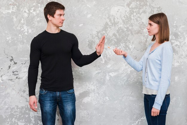 Young man saying no to woman offering cigarette standing near old wall