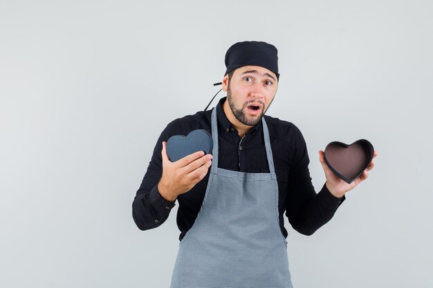 Young man in shirt, apron holding empty present box and looking surprised, front view.