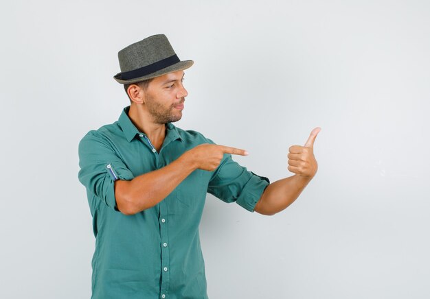 Young man in shirt, hat pointing at his thumb up