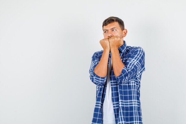 Giovane uomo in camicia tenendo i pugni sulla bocca e guardando spaventato, vista frontale.