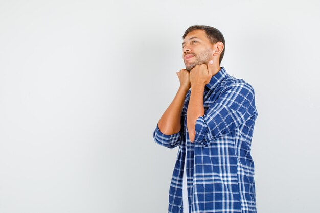 Young man in shirt holding hands under chin and looking hopeful , front view.