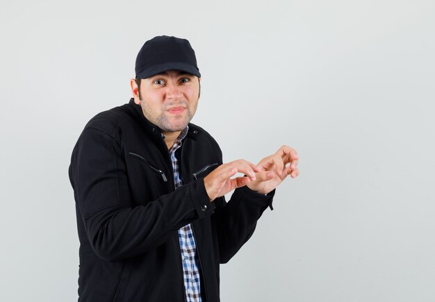 Young man in shirt, jacket, cap showing typing gesture with clenched fingers