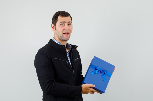 Young man in shirt, jacket holding present box and looking positive