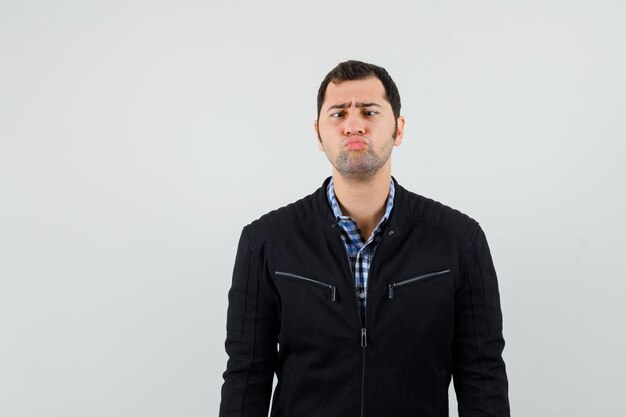 Young man in shirt, jacket keeping lips folded and looking gloomy