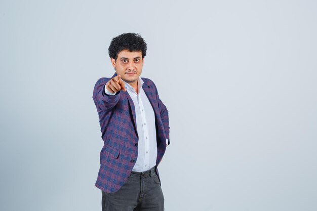 Young man in shirt, jacket, pants pointing at camera and looking confident , front view.