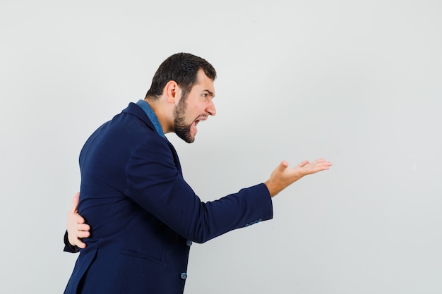 Young man in shirt, jacket shouting at somebody and looking angry .