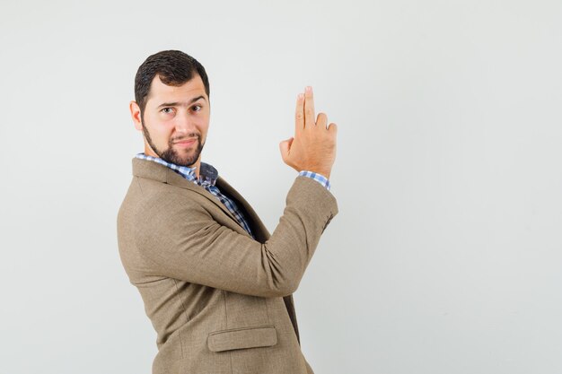 Young man in shirt, jacket showing gun gesture and looking confident .