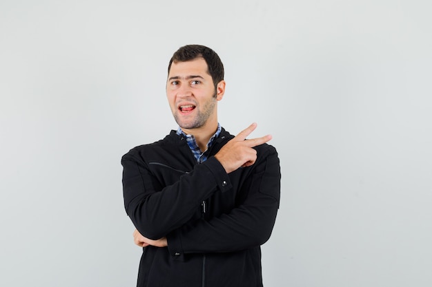 Young man in shirt, jacket showing victory sign and looking confident