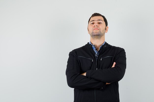 Young man in shirt, jacket standing with crossed arms and looking confident