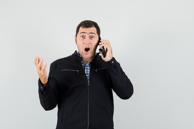 Giovane uomo in camicia, giacca parlando al cellulare e guardando stupito