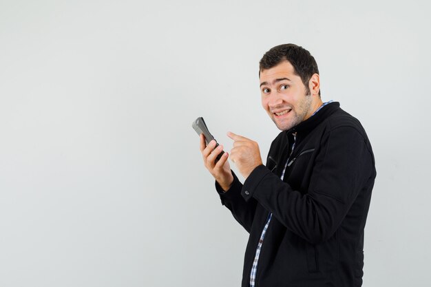 Young man in shirt, jacket using calculator and looking cheery