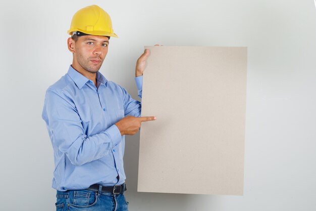 Young man in shirt, jeans, helmet pointing finger at canvas