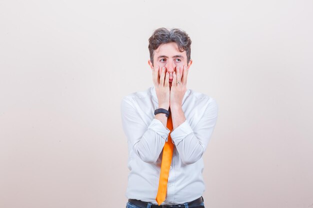 Young man in shirt, jeans holding hands on face and looking distressed