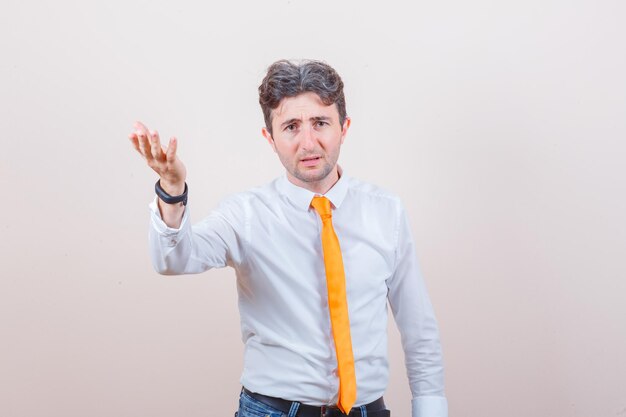 Young man in shirt, jeans raising hand in puzzled gesture