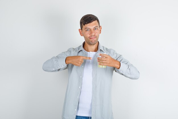 Young man in shirt, jeans showing juice glass with finger