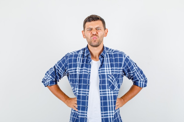 腰に手をつないで、暗い、正面図を見て、しかめっ面のシャツを着た若い男。
