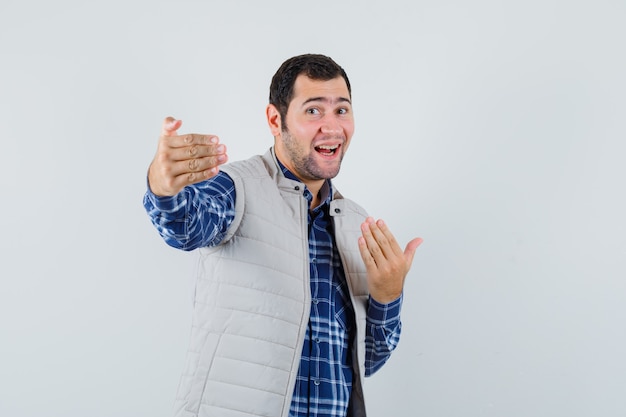 Free photo young man in shirt,sleeveless jacket inviting someone near him and looking joyful , front view.