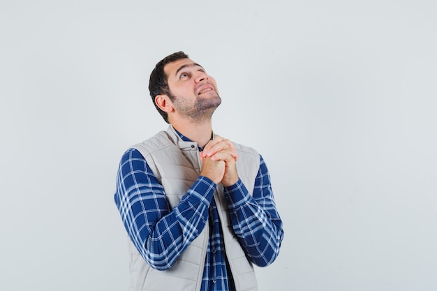 Giovane uomo in camicia, giacca senza maniche pregando per qualcosa e guardando speranzoso, vista frontale.