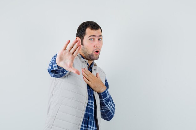 Young man in shirt,sleeveless jacket refusing something , front view.