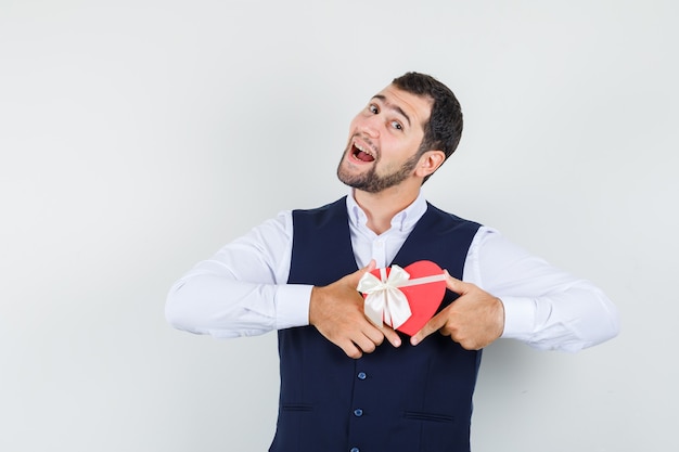 Foto gratuita giovane uomo in camicia, giubbotto tenendo presente la casella e guardando gioioso