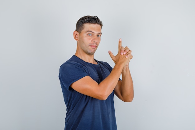 Young man shooting up with finger pistol in dark blue t-shirt front view.