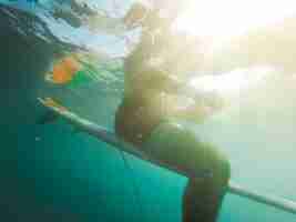 Foto gratuita giovane in pantaloncini seduto sulla tavola da surf nell'oceano