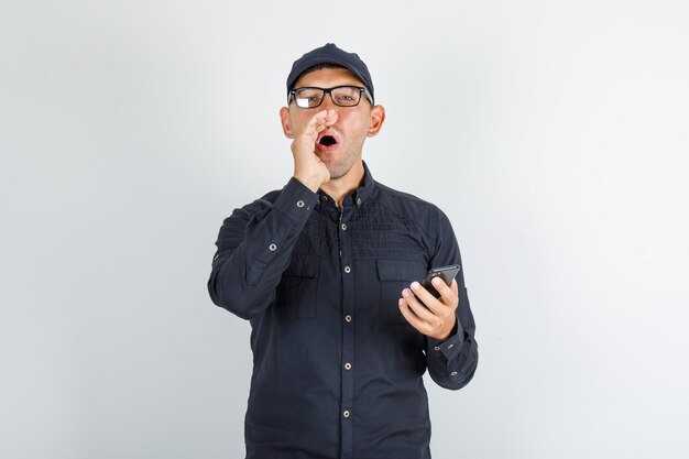 Young man shouting and holding mobile phone in black shirt with cap