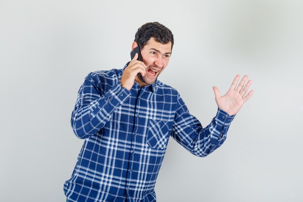 young man shouting on phone with stop sign in checked shirt and looking nervous