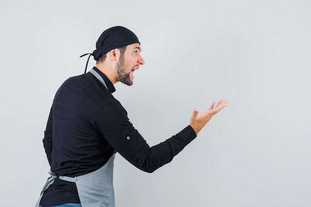 Young man shouting at somebody in shirt, apron and looking delirious. .