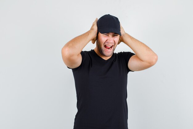 Young man shouting with hands on ears in black t-shirt