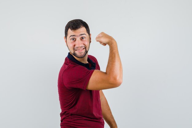 Young man showing arm muscle in red t-shirt and looking flexible , front view.