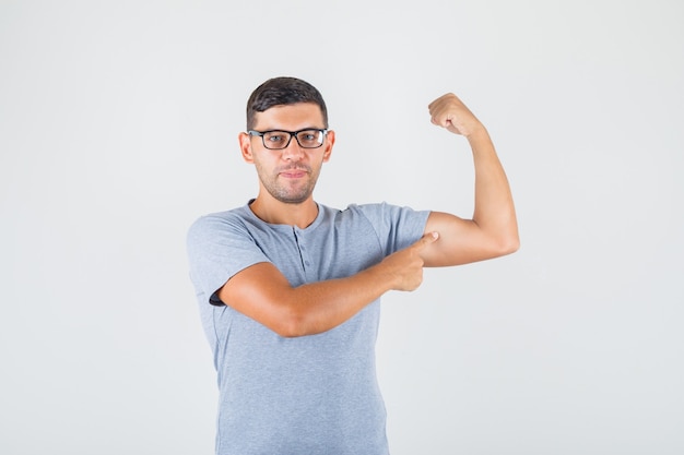 Young man showing biceps on his arm in grey t-shirt, glasses