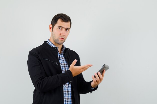 Young man showing calculator in shirt, jacket and looking sensible , front view.