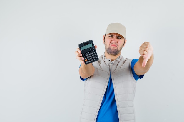 Бесплатное фото Молодой человек показывает калькулятор большим пальцем вниз в футболке, куртке и недовольным взглядом. передний план.