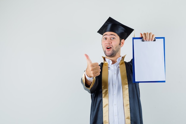 卒業式の制服を着て親指を立ててクリップボードを見せて、嬉しそうに見える若い男。正面図。