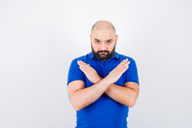 Young man showing closed gesture in blue shirt and looking focused , front view.