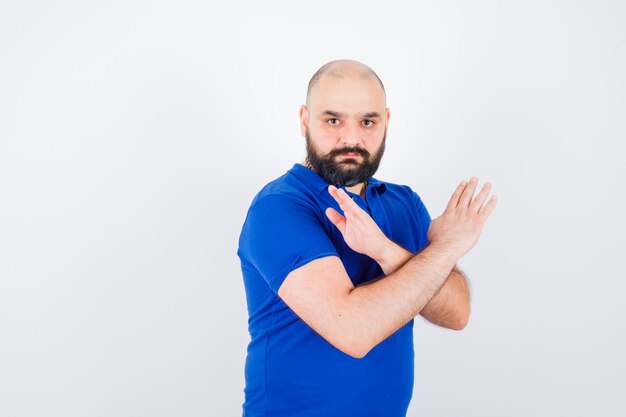 Young man showing closed gesture in blue shirt and looking serious. front view.