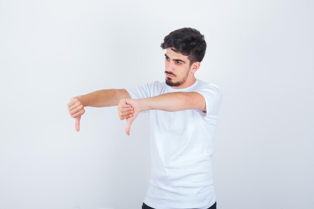 Young man showing double thumbs down in white t-shirt and looking confident