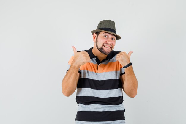 Tシャツ、帽子、陽気に見える二重親指を示す若い男。