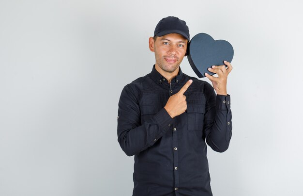 Foto gratuita giovane che mostra confezione regalo in camicia nera con cappuccio e sembra allegro