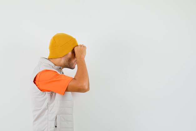 Young man showing glasses gesture in t-shirt, jacket, hat and looking focused .