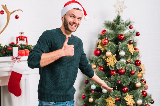 Young man showing good near Christmas tree