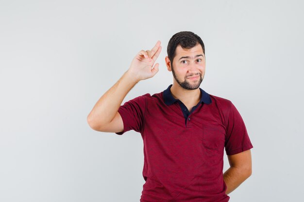 Young man showing goodbye gesture in red t-shirt and looking calm , front view.