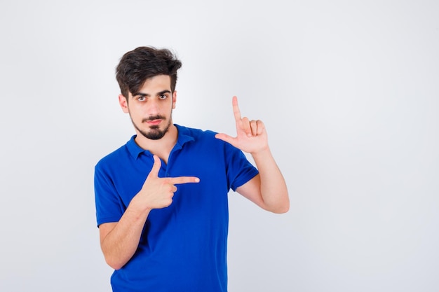 Young man showing gun gesture and pointing to it in blue t-shirt and looking serious