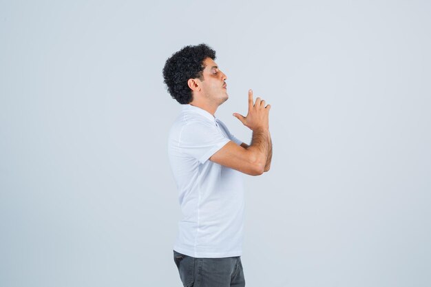 Young man showing gun gesture in white t-shirt and jeans and looking focused. front view.