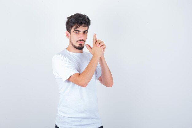 Young man showing gun gesture in white t-shirt and looking confident