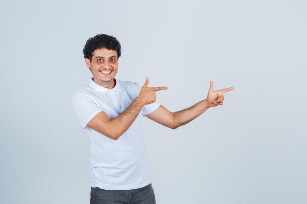 Young man showing gun gesture in white t-shirt, pants and looking confident. front view.