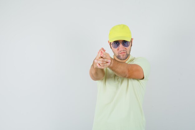 Young man showing gun gesture in yellow uniform and looking spiteful.